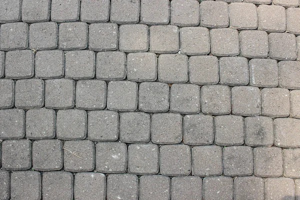 Dışarıdaki gri beton kaldırım bloklarında kare desen düz ve katı zemin yüzeyinde yinelenen bir dokuyu temsil ediyor..