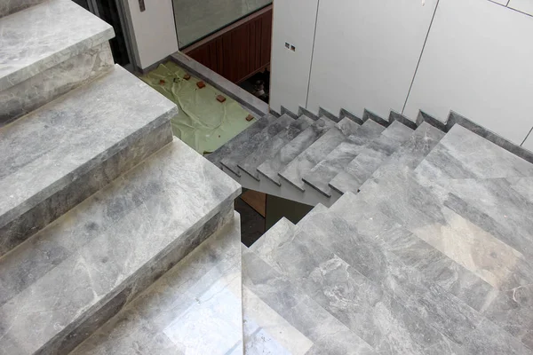 Top-down view of two flights of tiered gray marble stairs, highlighting the natural vein pattern and modern interior design of the house.