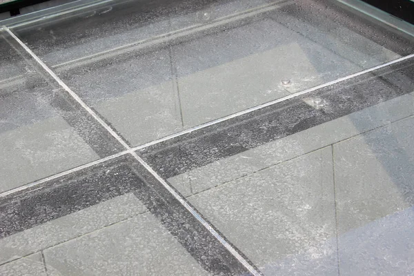 Close-up detail of glass roof panels showing condensation or water droplets on their surface and the cross seal between panels.
