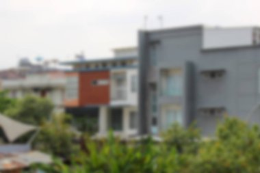 Soyut arkaplan odak dışı. Kentsel alanda üç modern minimalist yerleşim yeri, gri, beyaz ve ahşap aksanlı ön planda tropikal bitki örtüsüyle bulutlu bir gökyüzünün altında..