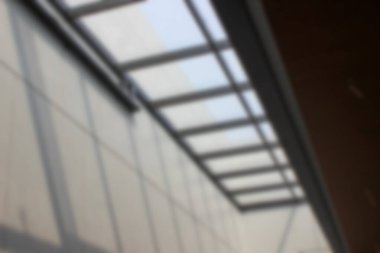 Soyut arkaplan odak dışı. Modern cam çatı penceresi koyu renk yatay çelik kirişlerle desteklenir, açık gri panel duvarlar üzerine kurulur, iç kısımda doğal ışık sağlar..