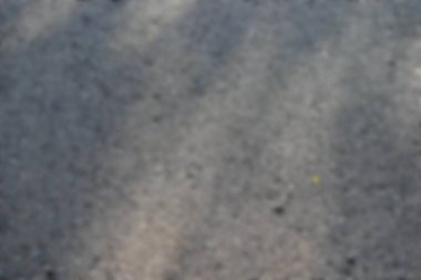 Soyut arkaplan odak dışı. Kaba taneli asfalt yüzeyin dokusu koyu gri ve siyah, güneş ışığıyla aydınlatılıyor ve gölgeler yaratıyor..
