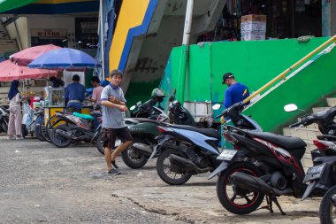 Jakarta, Endonezya - 20 Aralık 2025: Baskın yeşil ve sarı duvar renklerine sahip dükkanların önündeki motosiklet park alanı etrafında yerel etkinlik.