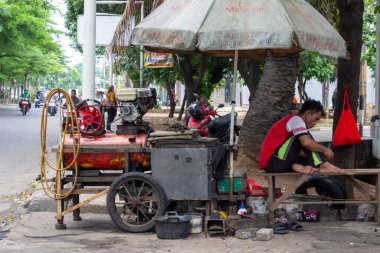 Jakarta, Endonezya - 20 Aralık 2025: Jakarta karayolu kenarında büyük bir şemsiye altında bir hava kompresörü motorunun yanında oturan bir lastik tamircisi.