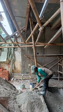 Jakarta, Endonezya - 20 Aralık 2025: İnşaat malzemeleri yapımında kum ve çimento karışımı karıştıran çizme giyen bir inşaat işçisi