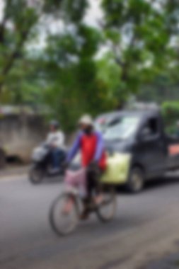 Soyut arka plan bulanık. Jakarta, Endonezya - 20 Aralık 2025: Motosiklet ve araba trafiği arasında bisiklet süren orta yaşlı bir adam.