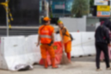 Soyut arkaplan odak dışı. Jakarta, Endonezya - 21 Aralık 2025: PPSU memurları veya turuncu askerler, Sudirman bölgesinde Mandiri BNI Bankası ve Etiqa logoları yakınlarındaki beton bariyerlerin arkasında dinleniyorlar.