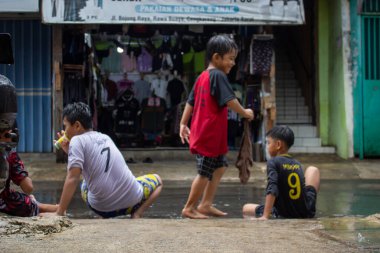 Jakarta, Endonezya - 01 Ocak 2026: Bir yerleşim bölgesindeki geleneksel bir giyim mağazasının önündeki sel basmış sokakta oynayan çocuklar.