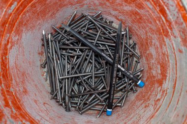 Temiz demir çiviler ve turuncu plastik bir kovanın içinde iki Joyko P-92 2B marka marangoz kalemleri..