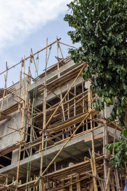 Jakarta 'daki yeşil ağaçların yanındaki modern bir inşaat projesinde kullanılan geleneksel bambu iskelesi manzarası.