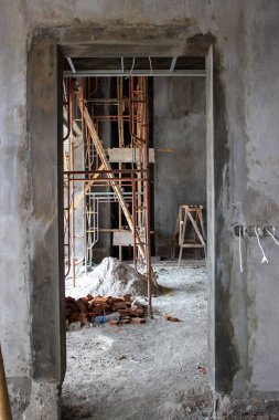 İnşaat halindeki binanın iç kısmında tuğla yığınları ve metal iskeleleri olan sert beton duvarlar görülüyor..