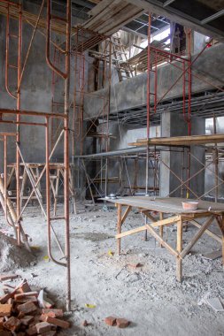 Yüksek çelik iskeleli büyük ölçekli bir inşaat projesinin iç şartları ve orta alanda malzeme kesmek için ahşap bir masa..