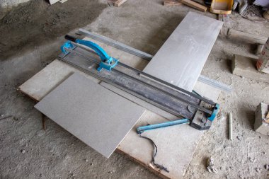 Bir proje alanındaki gri seramik parçaların yanına beton zemine elle kesme aracı yerleştirildi.