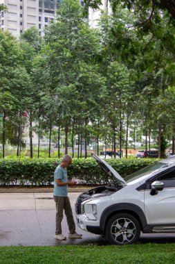 Tangerang, Endonezya - 10 Ocak 2026: Beyaz Mitsubishi Xpander arabasının motorunu kontrol eden bir adam Alam Sutera otoyolunun yanında kaput açık olarak bozuldu