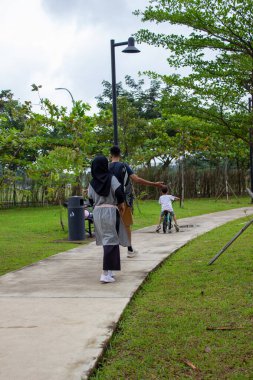 Tangerang, Endonezya - 10 Ocak 2026: Bir çift yetişkin yeşil Alam Sutera parkında yaya yolunda yürüyen bir çocuğun yanında yürüyor.