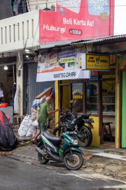 Jakarta, Endonezya - 18 Ocak 2026: Warteg Zehra 'nın önünde yürüyen yaşlı bir adam gıda ve Sidomuncul bitkisel ilaç satıyor.