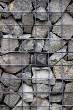 Koyu gri gabion taşından duvarın dikey dokusu ve toprak tutucu yapı takviyesi olarak demir tel örgüsü..