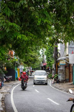 Jakarta, Endonezya - 18 Ocak 2026: Gölgeli Kembangan sokak kavşağından geçen gümüş renkli bir Daihatsu Xenia arabası ve motosikleti