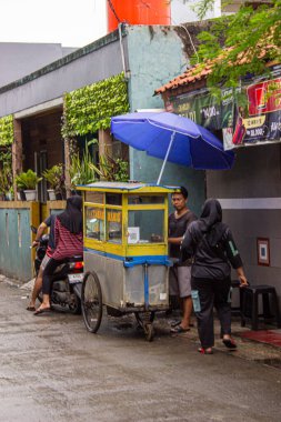 Jakarta, Endonezya - 18 Ocak 2026: Dar, ıslak bir caddenin kenarına park edilmiş sarı bir martabak yemek arabası.