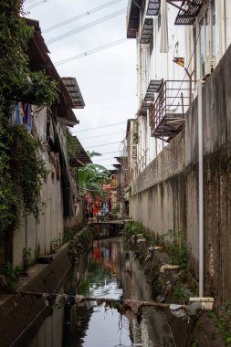 Jakarta, Endonezya - 25 Ocak 2026: Yüksek bina duvarları ile konut evleri arasındaki drenaj kanalı veya oluk manzarası.