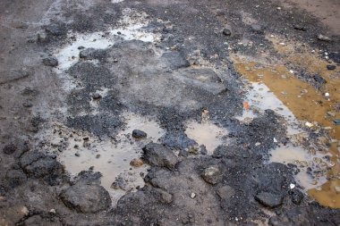 Ağır hasar görmüş asfalt yolu ve yoğun nüfuslu bir yerleşim bölgesinde su birikintileriyle dolu çukurların durumu.