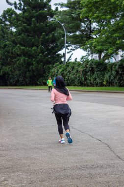 Jakarta, Endonezya - 25 Ocak 2026: Tesettür ve pembe spor giysileri giyen bir kadın, sabah asfalt bir sokakta konut alanında koşuyor.