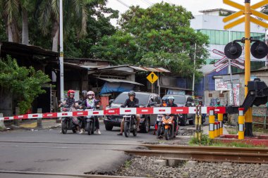 Jakarta, Endonezya - 25 Ocak 2026: Jakarta 'da kapalı bir demiryolu geçidinin önünde duran motosikletliler ve arabalar.