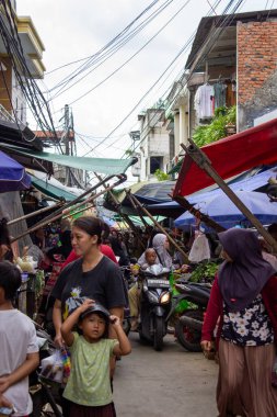 Jakarta, Endonezya - 25 Ocak 2026: Konukların ve motosikletlerin brandaların altından geçtiği kalabalık bir geleneksel pazarın atmosferi.