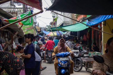 Jakarta, Endonezya - 25 Ocak 2026: Dar bir geleneksel pazar koridorunda mavi motosiklet kullanan bir kadın.