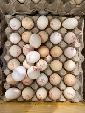 Kemik beyaz ve krem kabuklu bedava tavuk yumurtası Gallus gallus domesticus. Kalite işaretleyici olarak kırmızı pullar var.