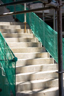 Jakarta, Endonezya - 16 Mart 2026: Yeşil koruyucu ağ ile kurulmuş yüksek katlı bir inşaat projesindeki sert beton merdivenlerin ayrıntıları.