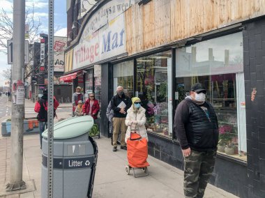 İnsanlar COVID-19 salgını sırasında mağazaya girmek için kuyrukta beklerken sosyal mesafeyi çalışırlar.