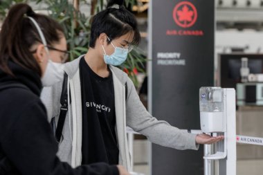 Gezgin, COVID-19 salgını sırasında Toronto 'daki Pearson Uluslararası Havalimanı' na giriş yapmadan önce el sanitzeri uyguluyor. El dezenfektanı takmak ve maske takmak artık havaalanında zorunlu..