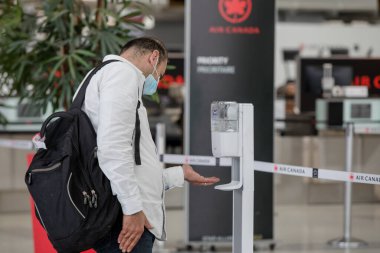 Yolcu, COVID-19 salgını sırasında Toronto Pearson Uluslararası Havalimanı 'na giriş yapmadan önce el dezenfektanı uyguluyor. El dezenfektanı takmak ve maske takmak artık havaalanında zorunlu..