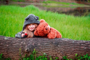 Bir oyuncak ayı bir glade üzerinde kızla bir ağacın arkasından dikkat.