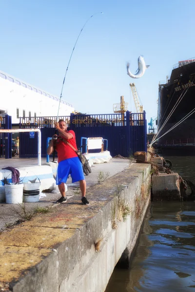 Rybář parmice. Boy rybářské parmice s barel na platformě průmyslového přístavu. V pozadí, podnik na opravu lodí v potrubí. — Stock fotografie