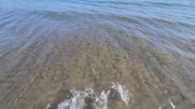 Şeffaf ve kristal berrak deniz suyu yüzeyi, deniz sahilde küçük dalgalar oluşturur.. 