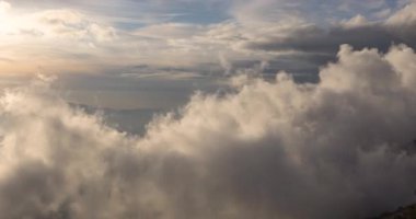 Dağların tepelerinde hareket eden bulutlar, ılık günbatımı ışığı olan bir sahne.