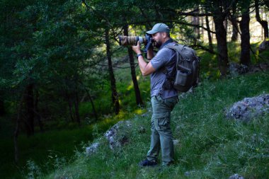 Ormandaki bir doğa fotoğrafçısı telefoto lensleriyle fotoğraf çekiyor. Adam, tam formunda, kamerayı gözüne doğru kaldırır ve tıklatır..