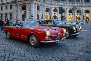 Roma, İtalya - 17 Ocak 2026: Kırmızı bir vintage Alfa Romeo ve klasik bir Lancia Piazza della Sahne, günlük hayata entegre edilmiş İtalyan otomotiv tasarımının zamansız zarafetini yakalıyor.