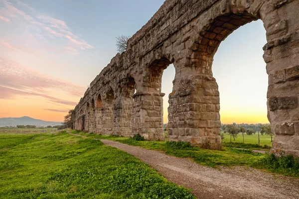 Römisches Aquädukt - Bögen eines antiken römischen Aquädukts aus Tuffsteinblöcken. ein weg verläuft entlang des grundstücks in einem grünen park am rand von rom. — Stockfoto