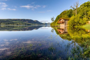 İngiltere 'nin Lake District bölgesindeki Ullswater Gölü' nü çevreleyen kayıkhane ve dağların net yansımaları..