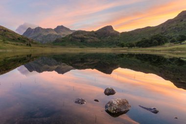 Gölde kayalarla yansıtılan ilahi yansımalarla canlı bir gün doğumu. Blea Tarn, Lake District, İngiltere.