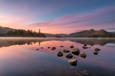 Güneş doğmadan önceki güzel pembe ve mor gün doğumu göldeki yansımaları yansıtıyor. İngiliz Göl Bölgesi 'ndeki Derwentwater' da çekilmiş..