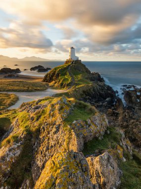 Anglesey Sahili, Galler, İngiltere 'deki Llanddwyn Deniz Feneri' nde kayaların üzerinde altın sabah ışığı..