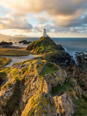 Golden morning light on rocks at Llanddwyn Lighthouse on the Anglesey Coast, Wales, UK. clipart