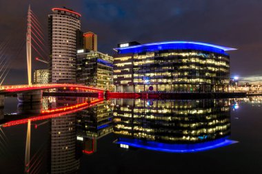 Aydınlatılmış ofis binaları İngiltere 'nin Salford Quays kentindeki modern köprüyle rıhtım kıyısına yansıdı..