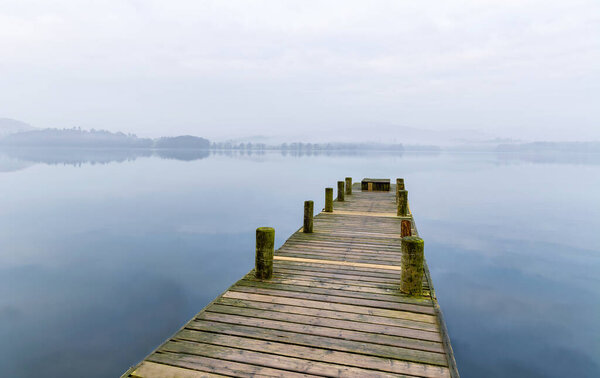 Long wooden jetty on a misty spring morning at Windermere in the Lake District, UK.