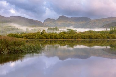 Gölde ve dağ zemininde mükemmel yansımalarla huzurlu puslu bir sabah. Lake District, İngiltere.