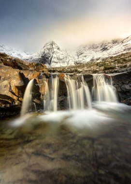 Beautiful Winter scene at the Fairy Pools on the Isle of Skye in the Scottish Highlands with snowcapped mountains and long exposure waterfall in the foreground. clipart